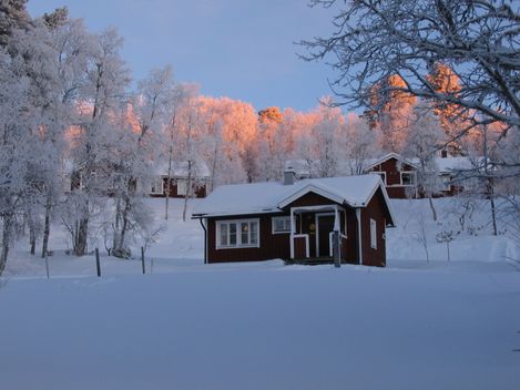 Röd fjällstuga i snötäckt landskap. Boka boende i Grövelsjön med Grövelsjögårdens stuguthyrning